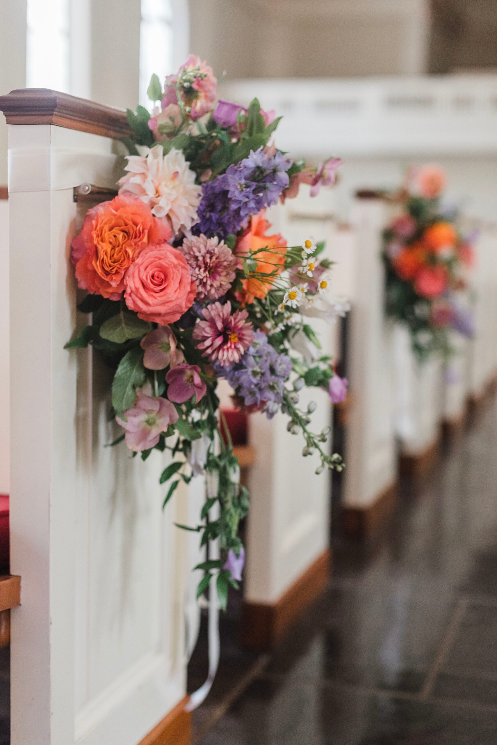 flower arrangements with pop of pastel colors decorate church pews 