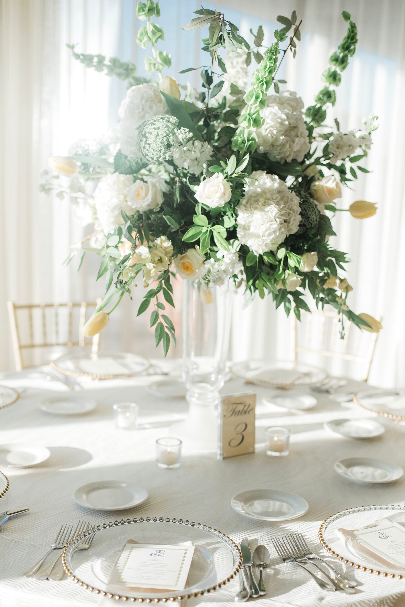 fresh white blooms and greenery in clear vases in the center of round table at rehearsal dinner