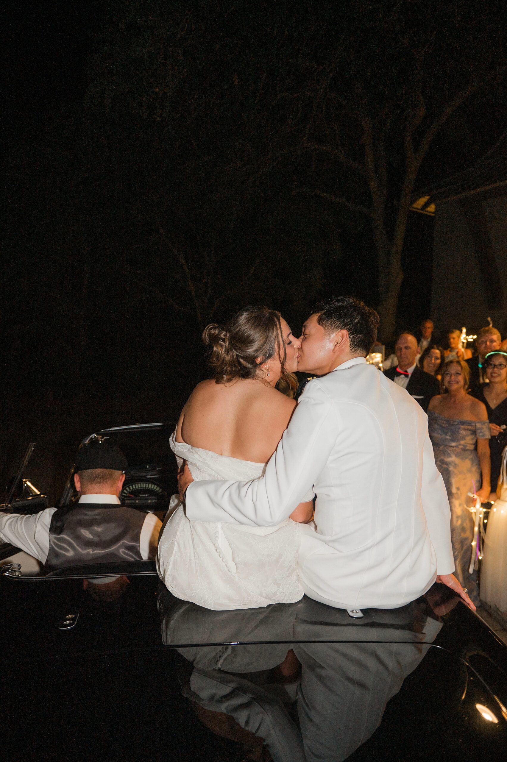 newlyweds kiss as they sit on back of convertible