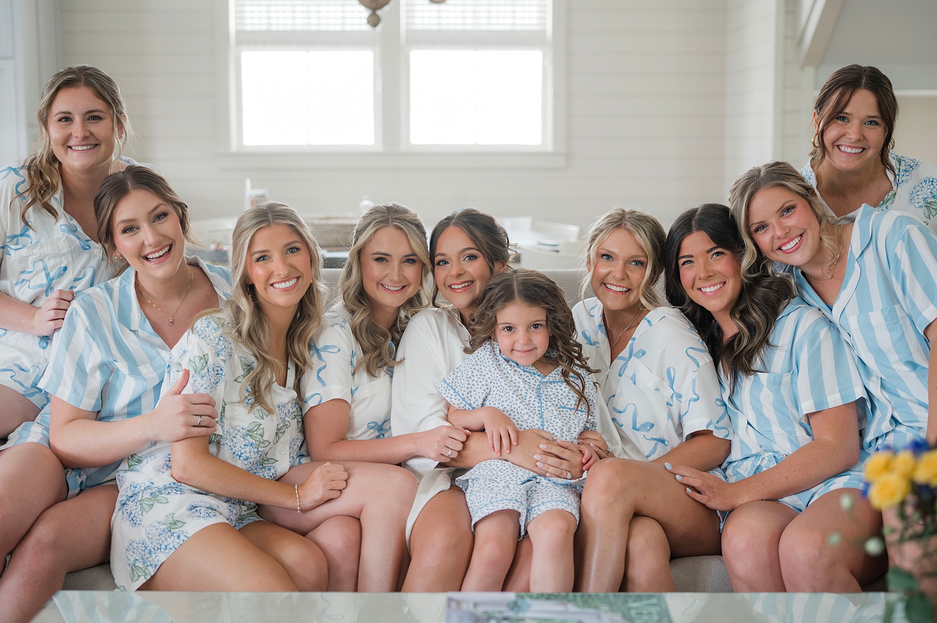 bride holds flower girl as bridesmaids sit around them in matching pjs