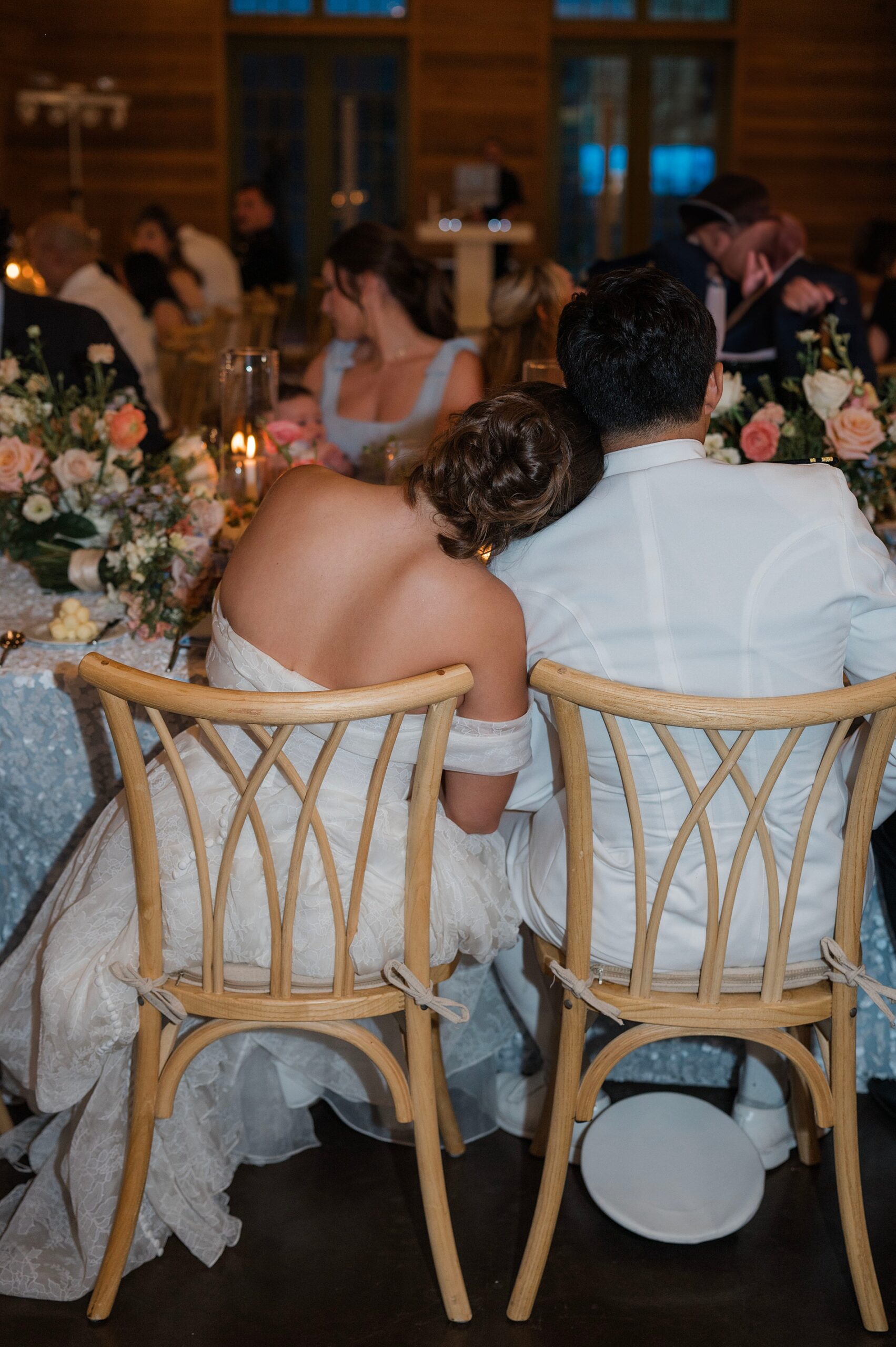 bride rests head on grooms shoulder as they sit together at wedding reception in 30A Florida
