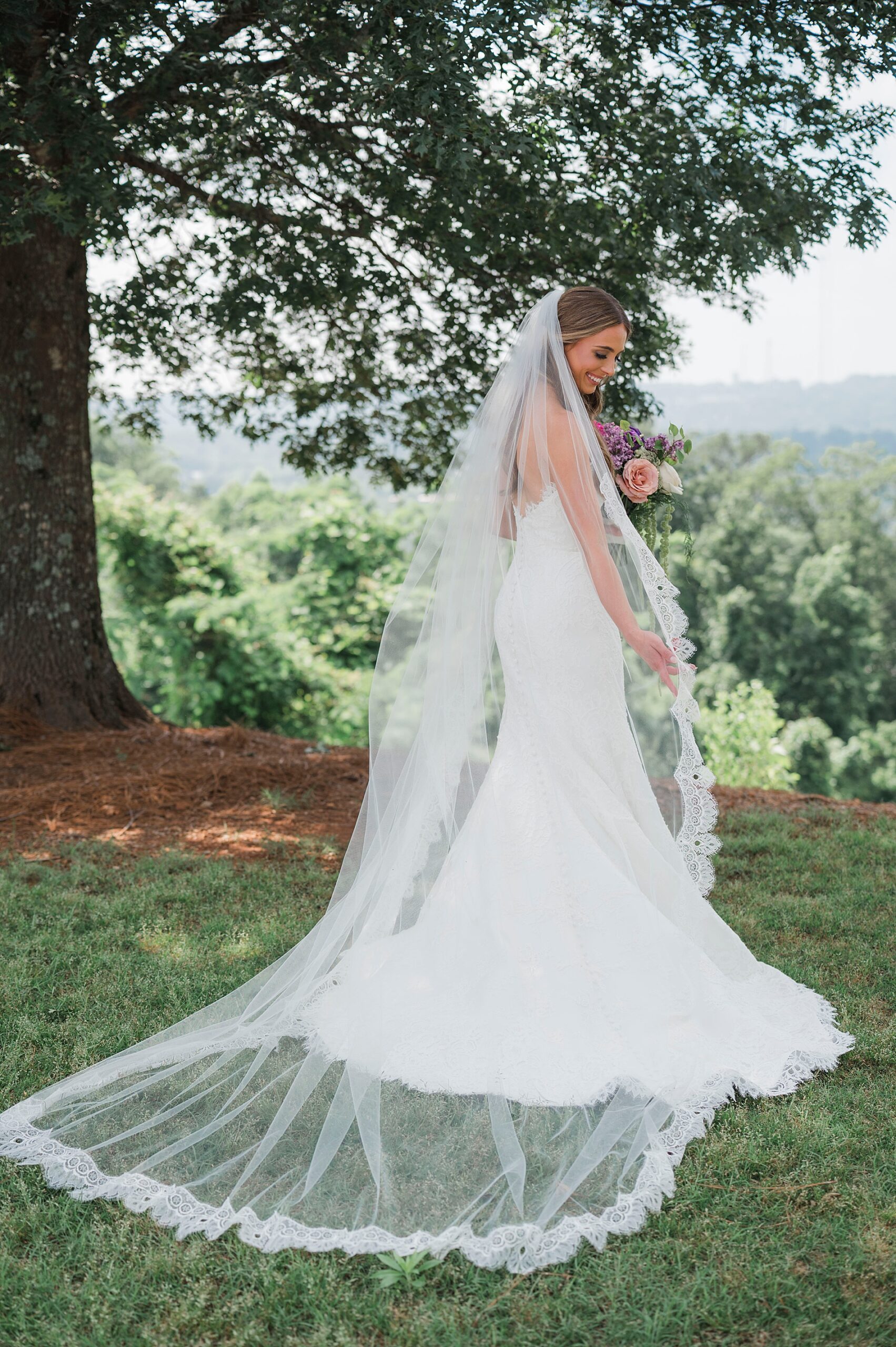 bride shows off back of wedding dress and cathedral length veil