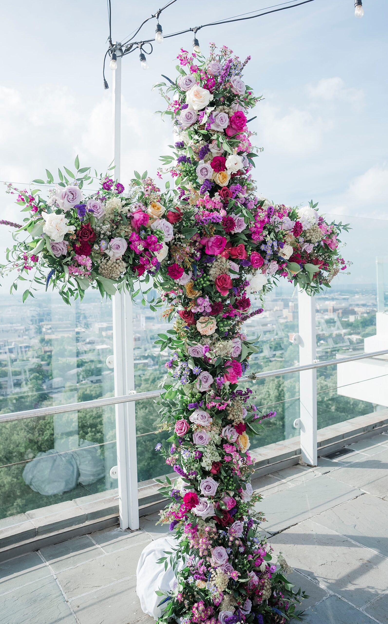 gorgeous wedding ceremony display of cross covered in greenery and white and purple flowers