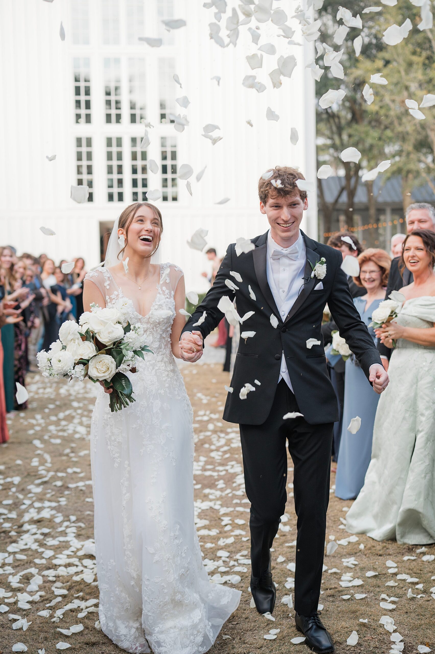 newlyweds exit while guests throw white flower petals 