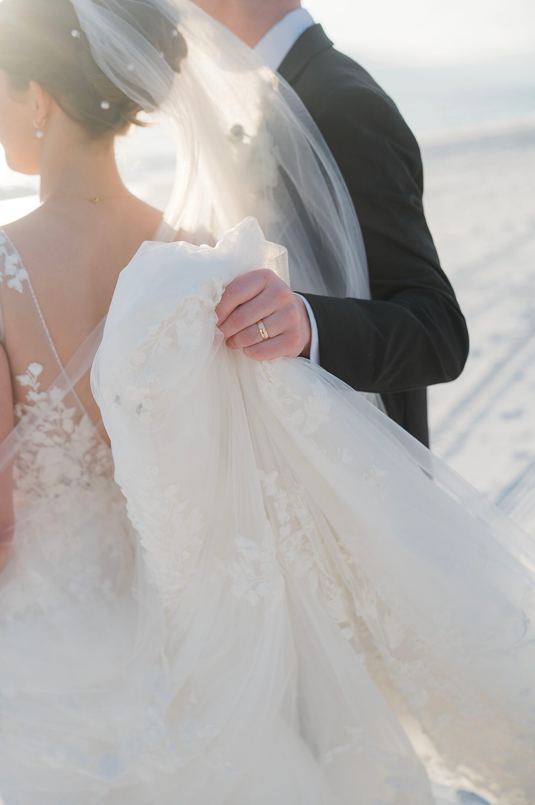 groom helps carry bride's dress across the beach 