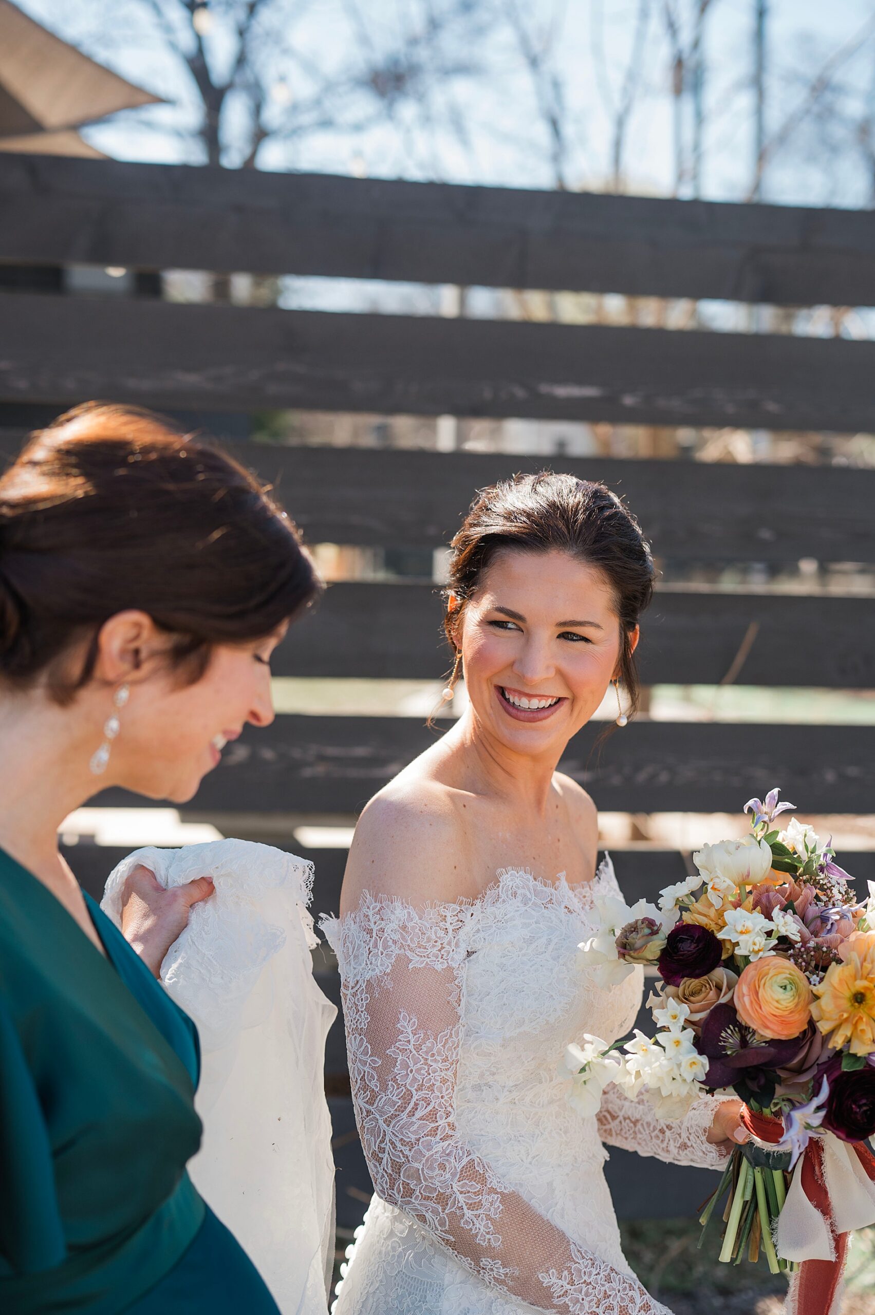 bridesmaid helps bride hold up the bottom of her wedding dress while walking outside