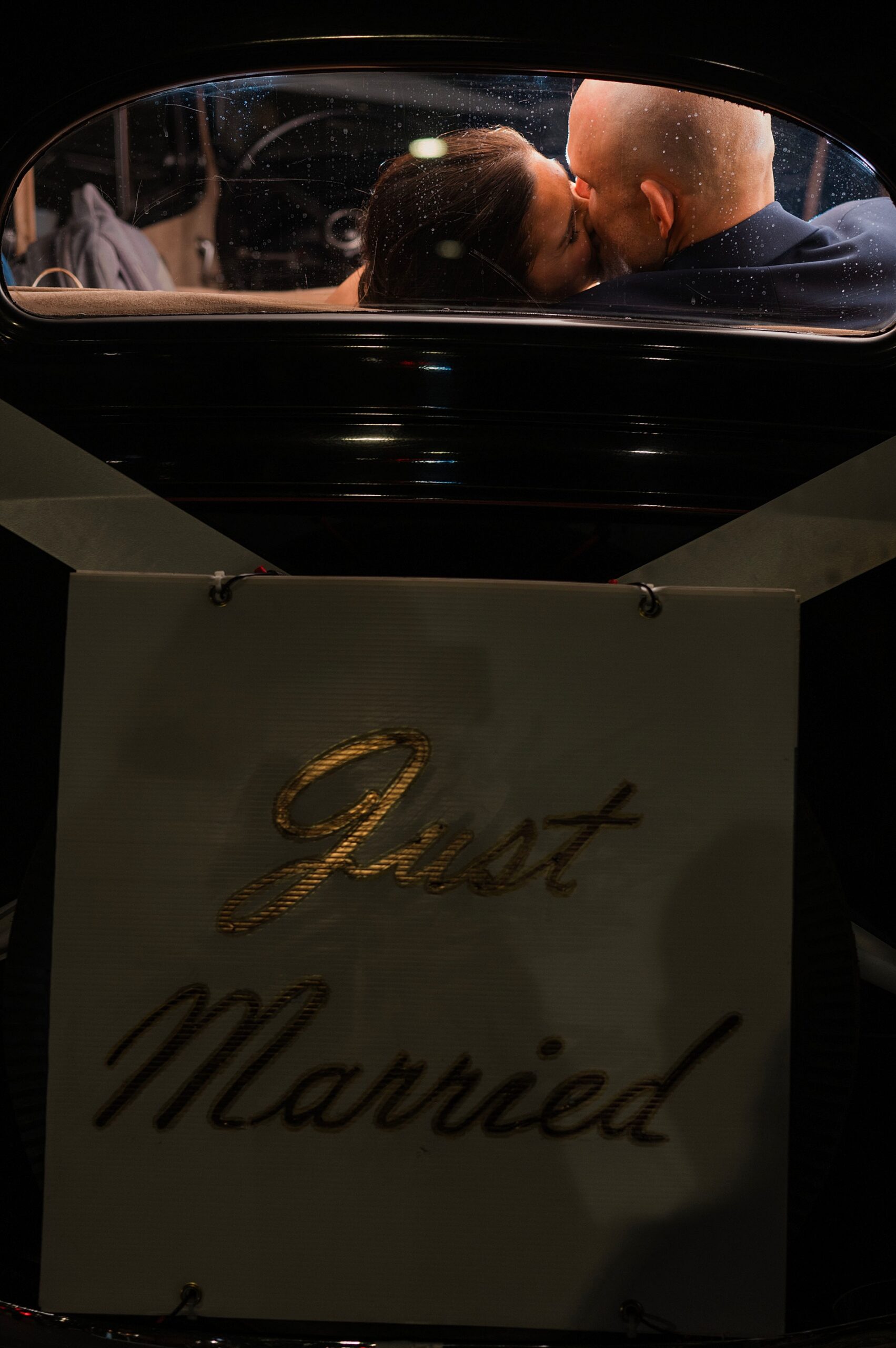 newlyweds kiss in back of classic car after leaving Classic Birmingham Winter Wedding at The Fennec