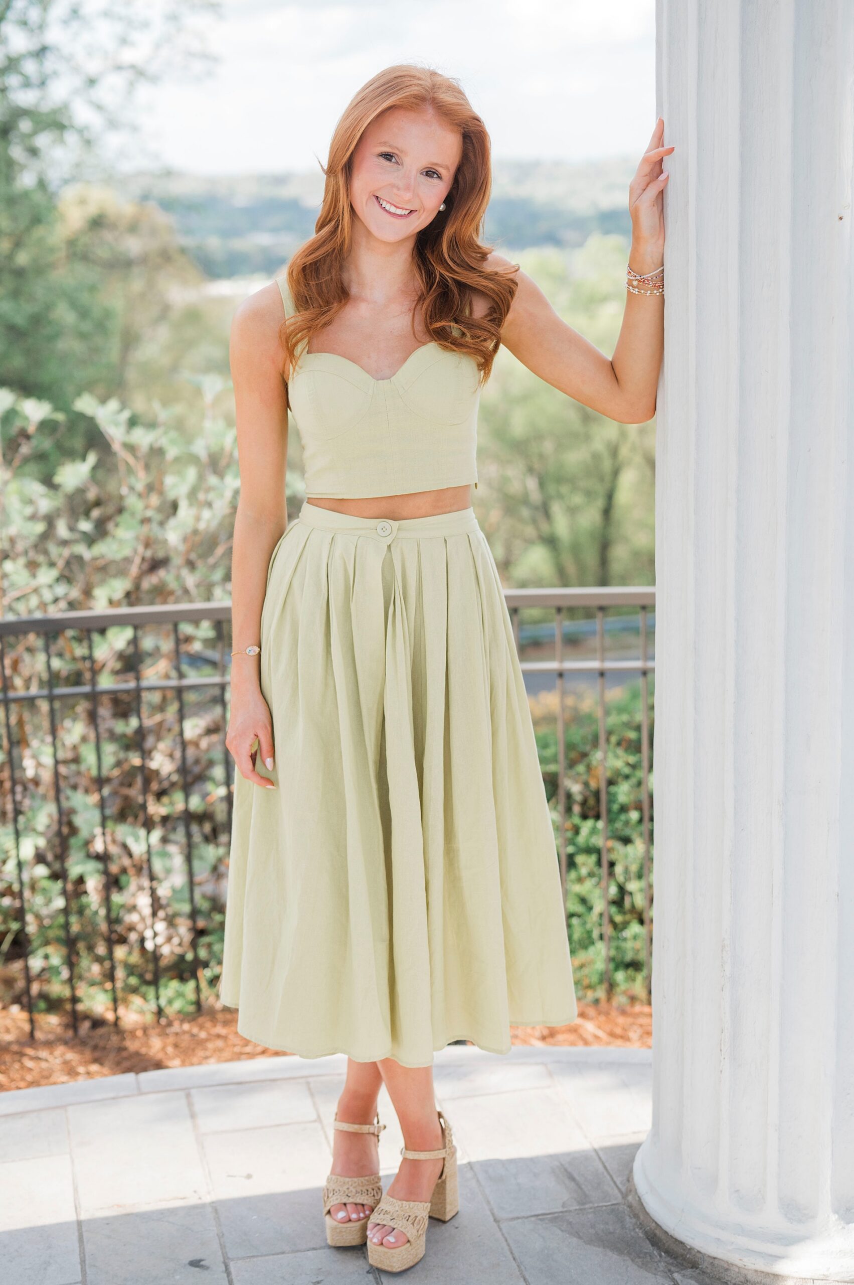 senior girl leans against column with garden behind her