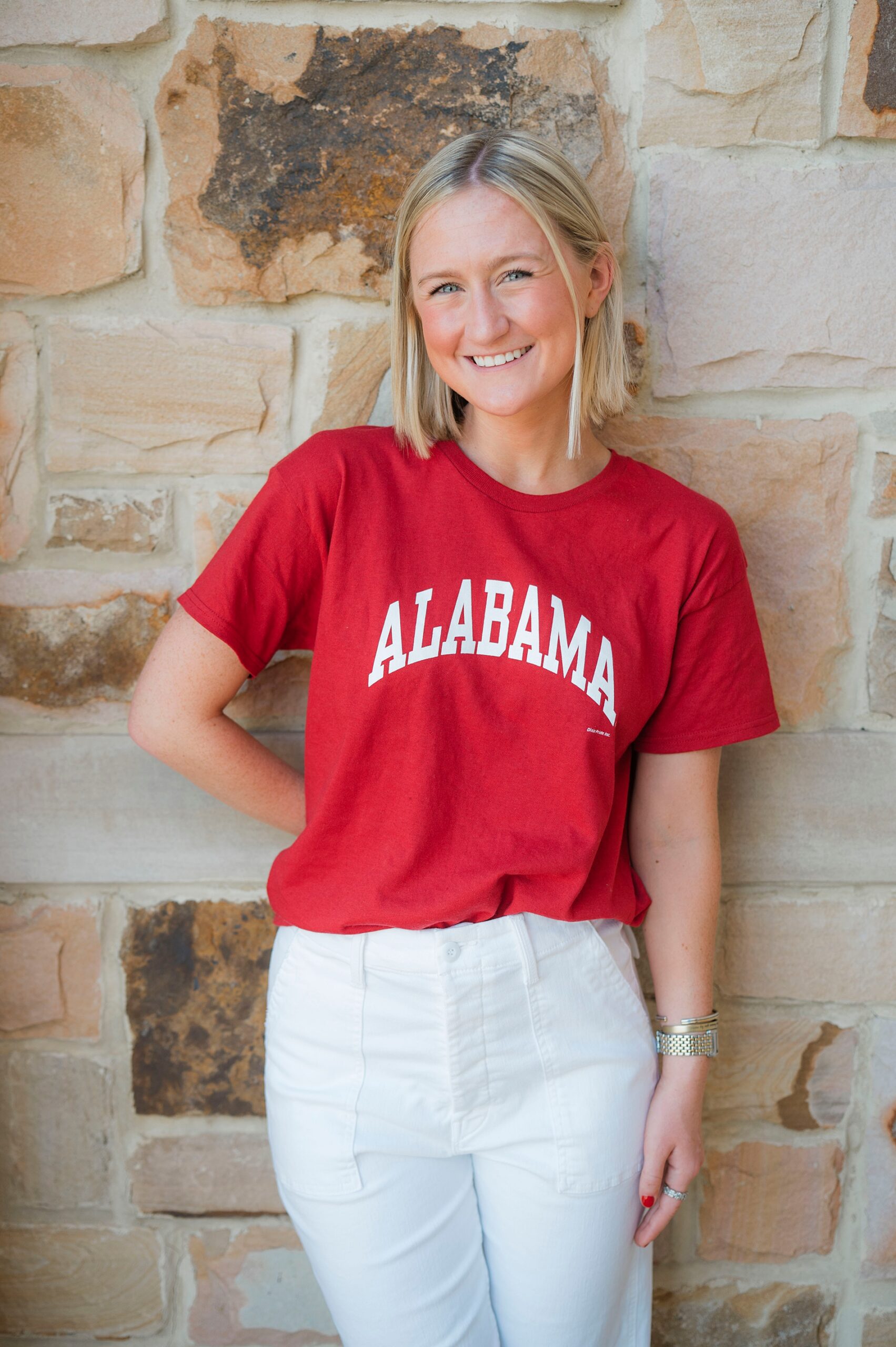 senior girl leans up against stone wall with read "Alabama" shirt on 
