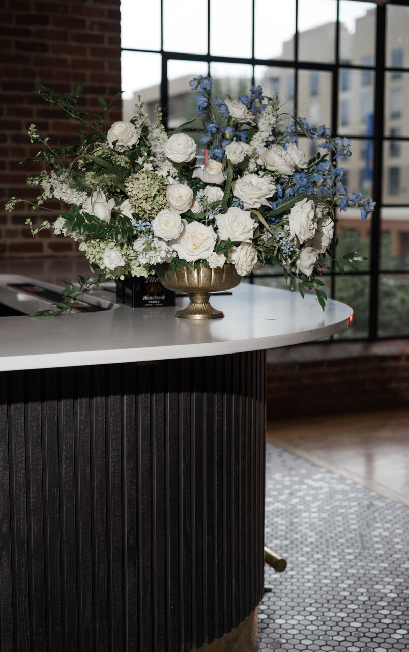 flower arrangement with white roses and blue flowers sit on bar