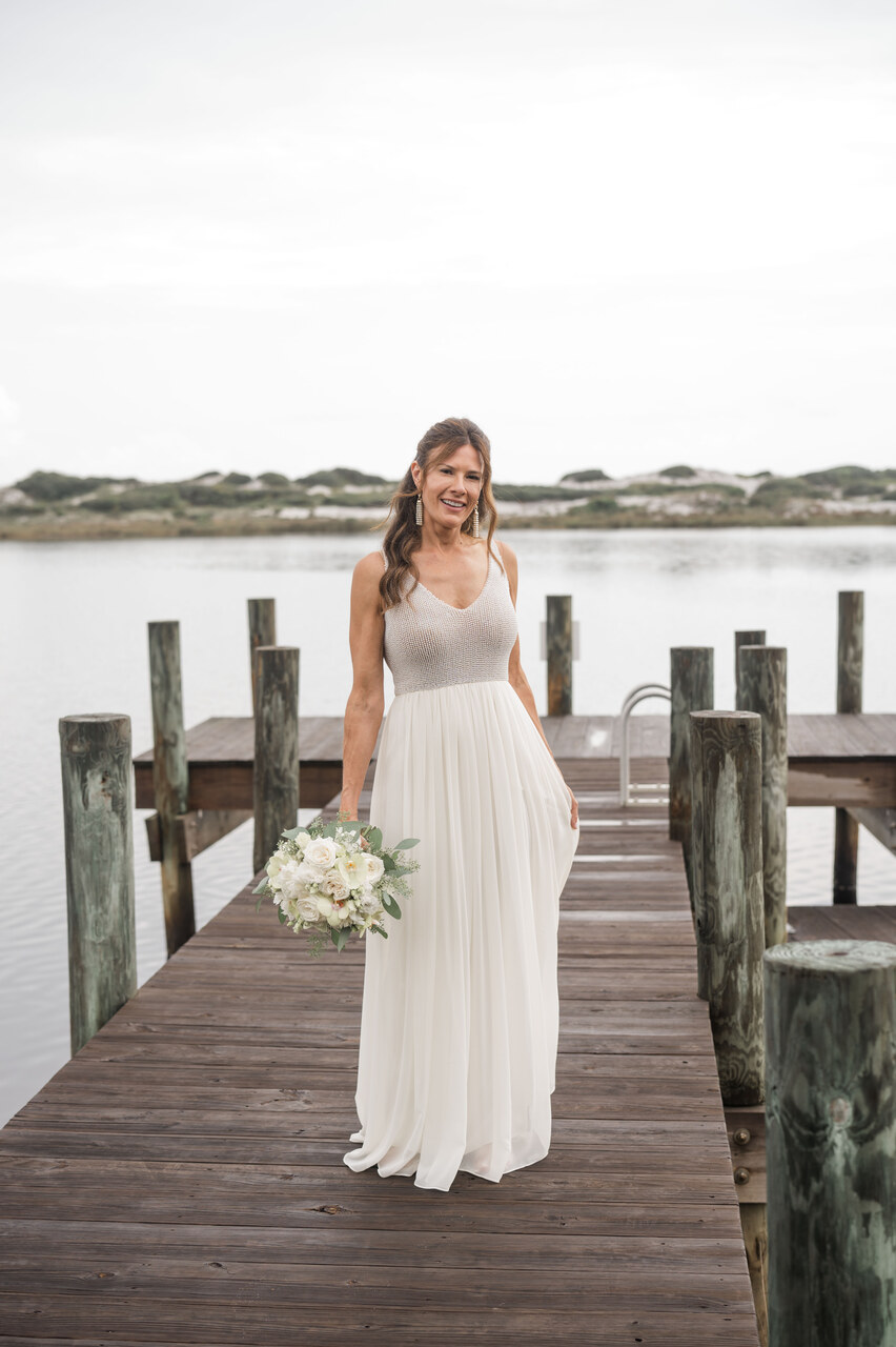bride in wedding dress stands on the dock by water in 30A