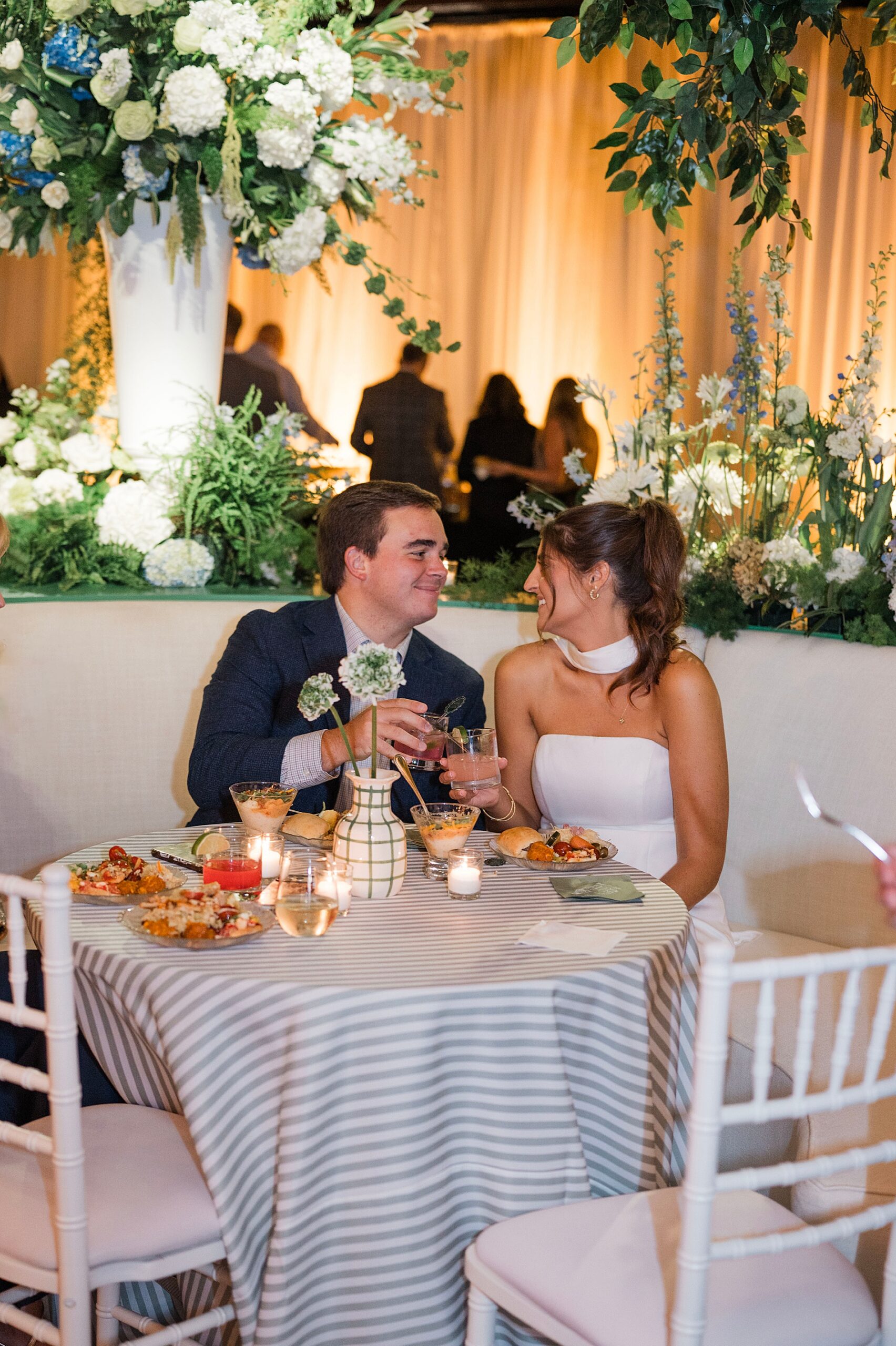 bride and groom sit together at table and share a toast 